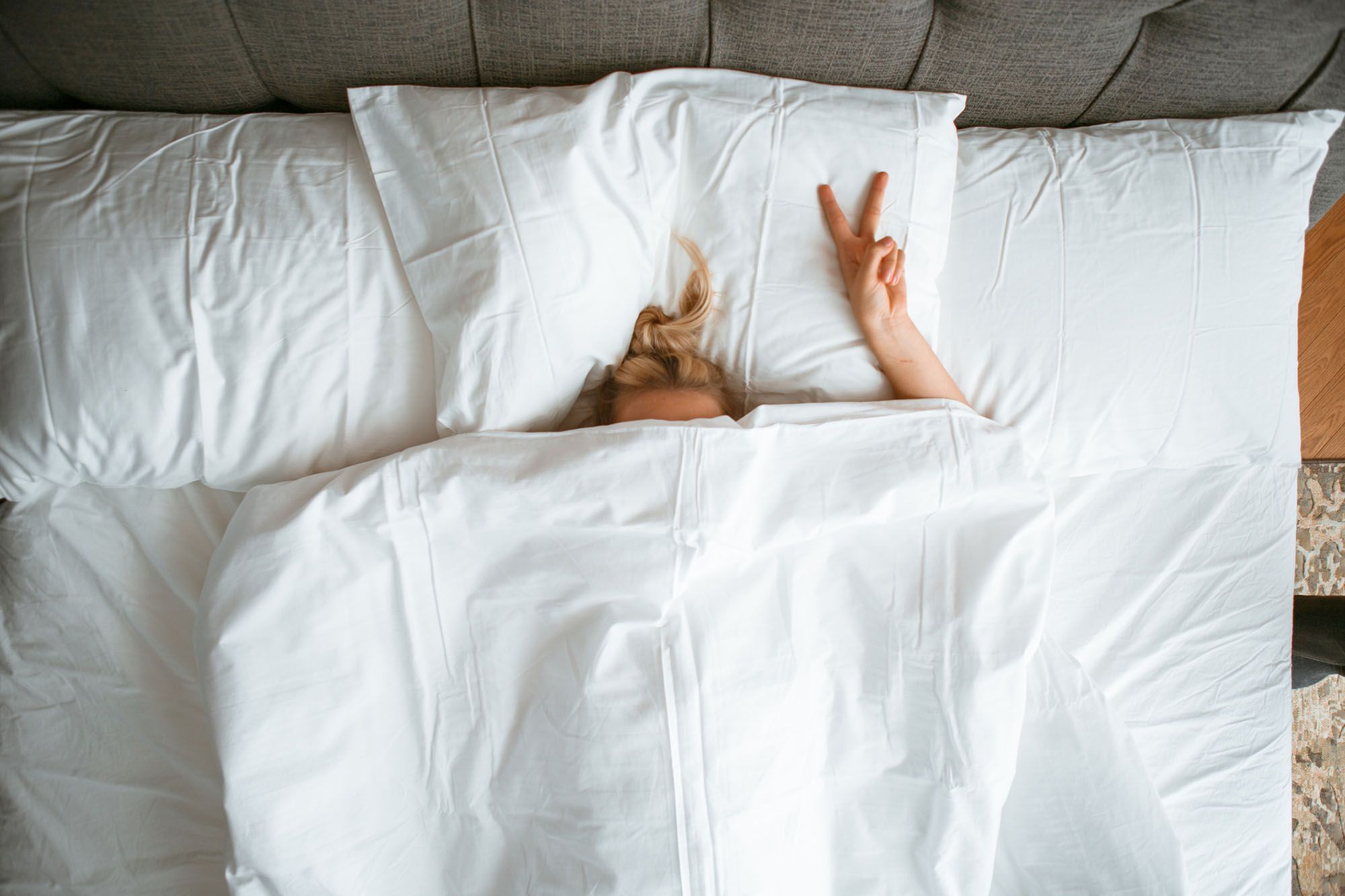 Frau liegt im Bett, nur der halbe Kopf und eine Hand schauen unter der Decke hervor