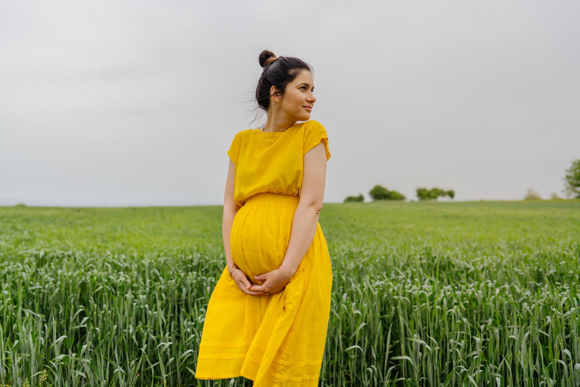 Schwangere Frau steht in einem Feld und hält ihren Babybauch