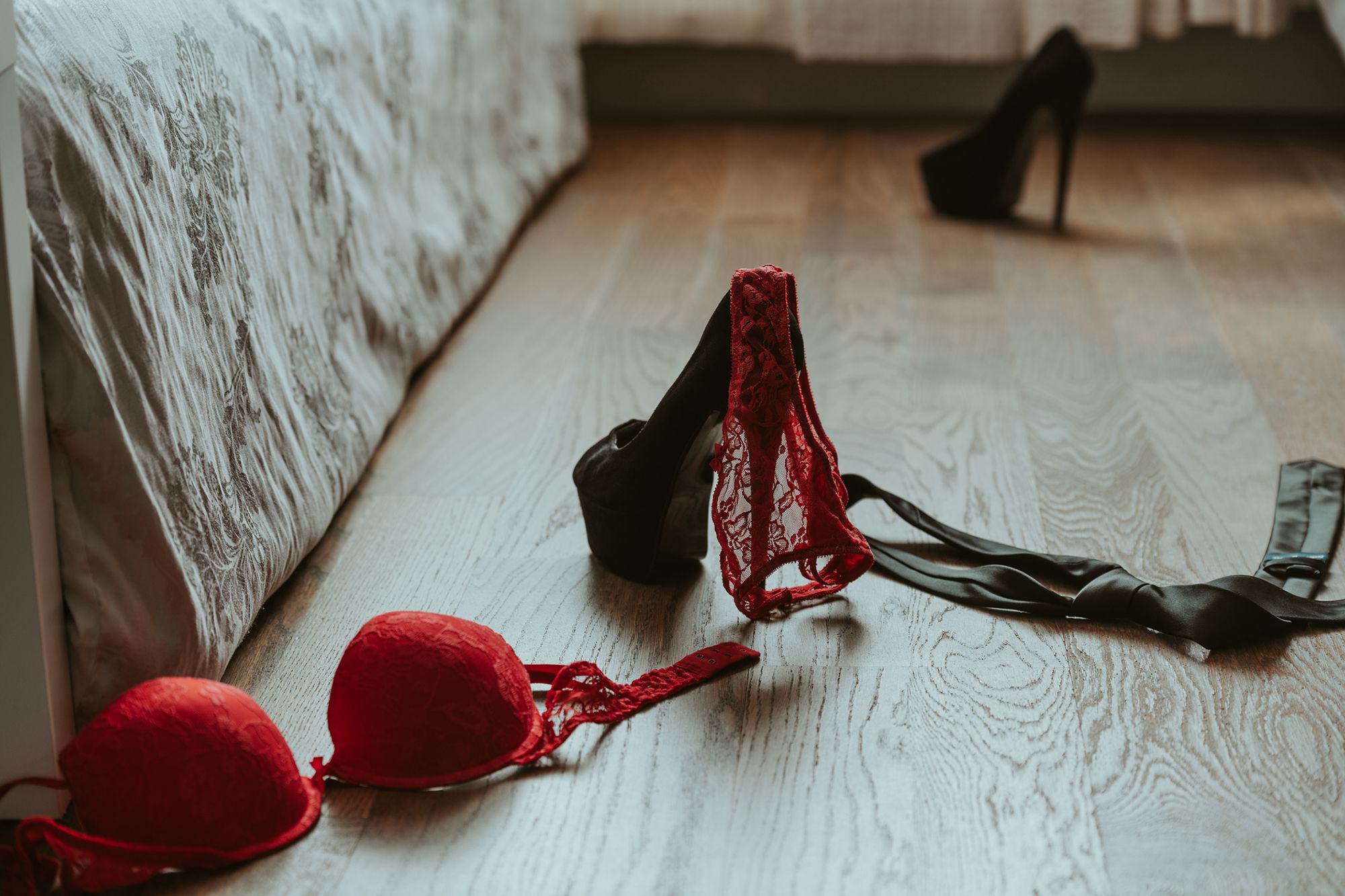 High Heels und rote Dessous auf dem Boden neben einem Bett