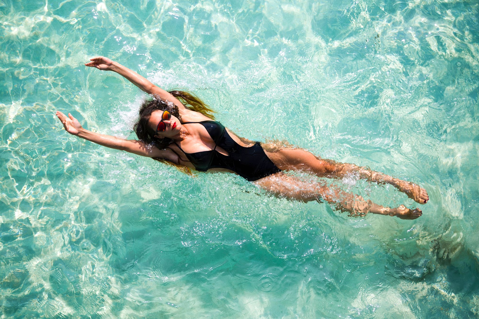 Frau mit schwarzem Badeanzug, die in einem Pool auf dem Rücken schwimmt