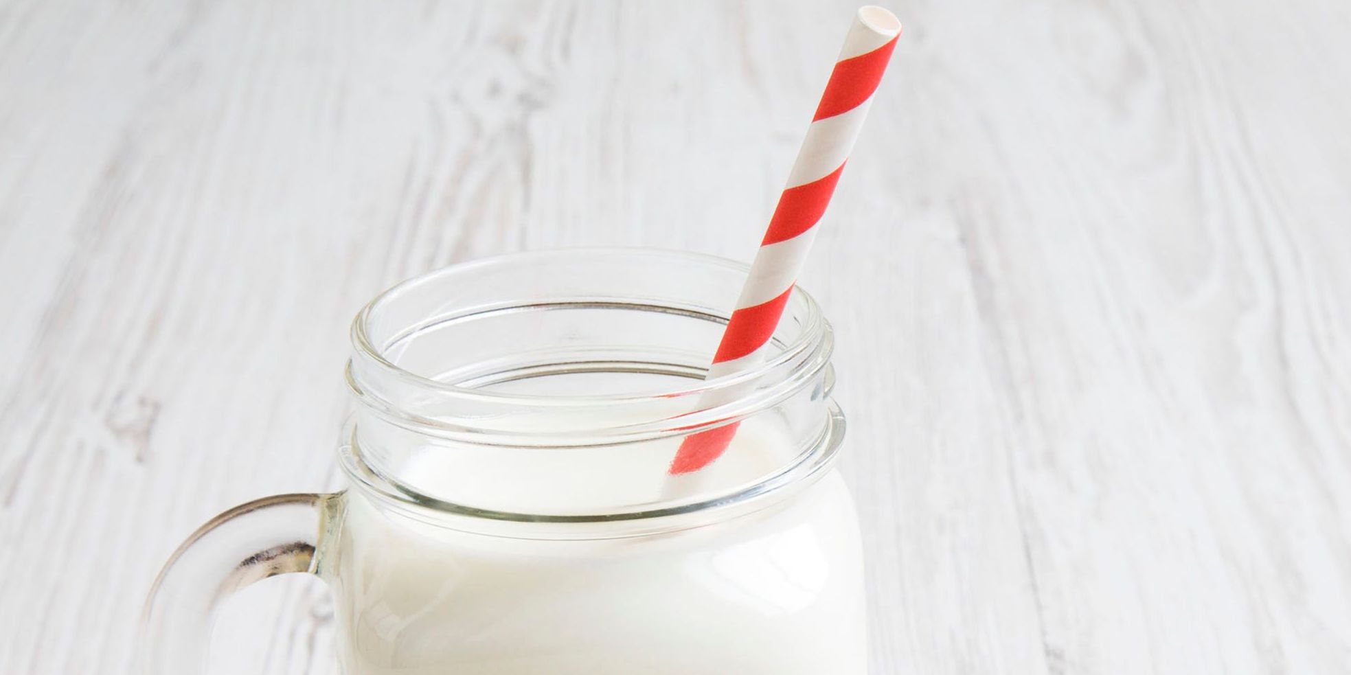 Glas mit Milch, in dem ein rot-weißer Strohhalm steckt