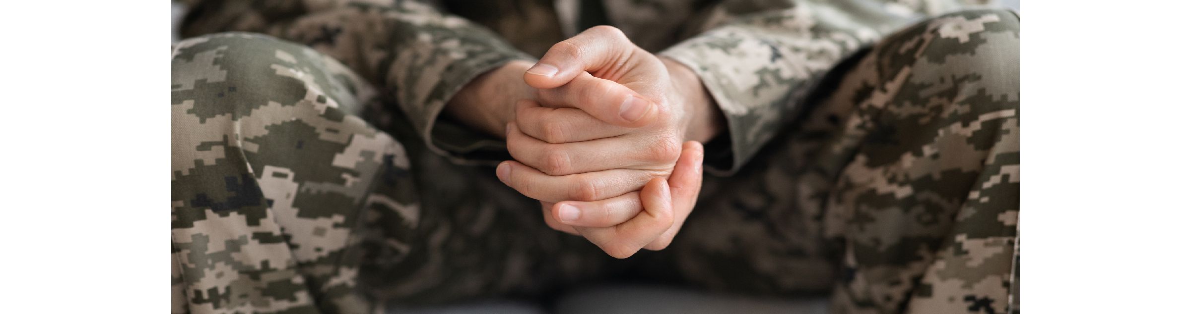 Eine Person in Tarnkleidung hat die Hände zwischen den Beinen zusammengeschlagen