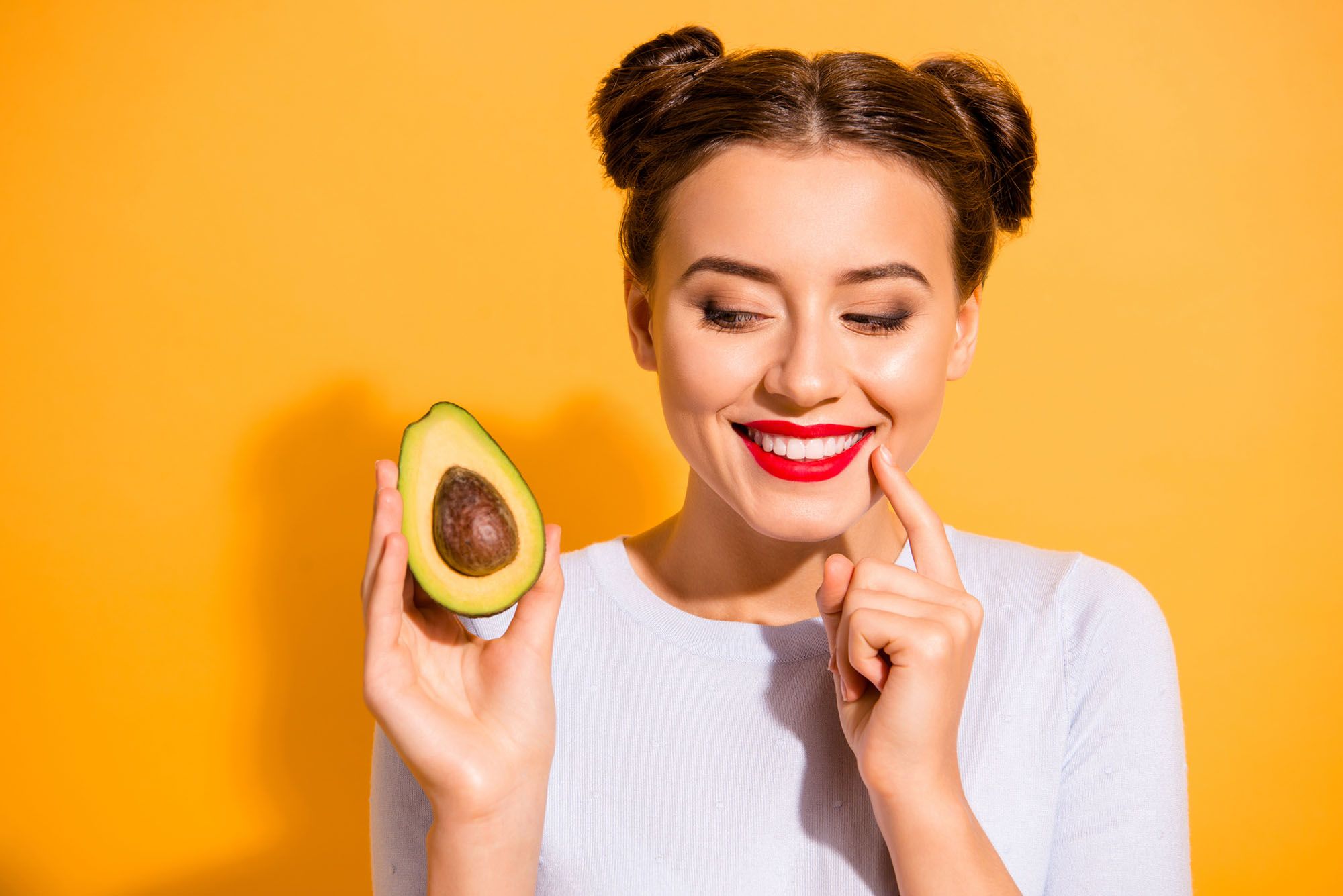 Frau, die eine halbe Avocado in der Hand hält und lächelt