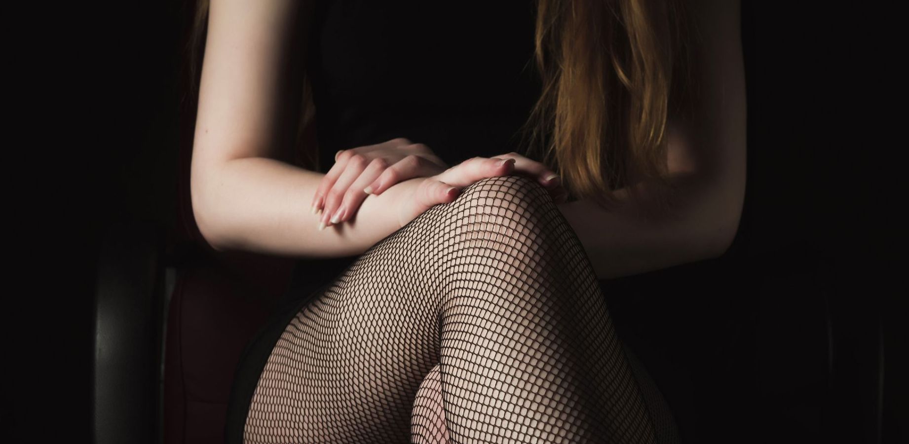 Domina Telefonsex - Abbildung einer Frau in schwarzem Kleid und Netzstrumpfhose mit überschlagenen Beinen