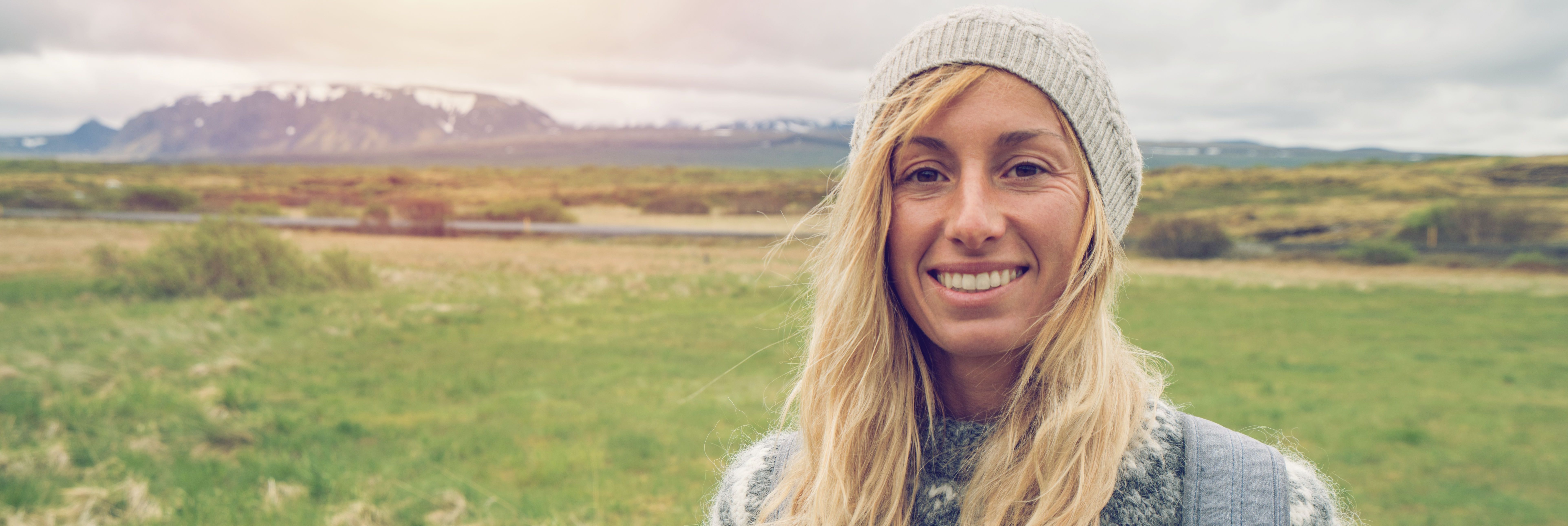 Junge Frau mit Mütze und blonden Haaren in einer Landschaft