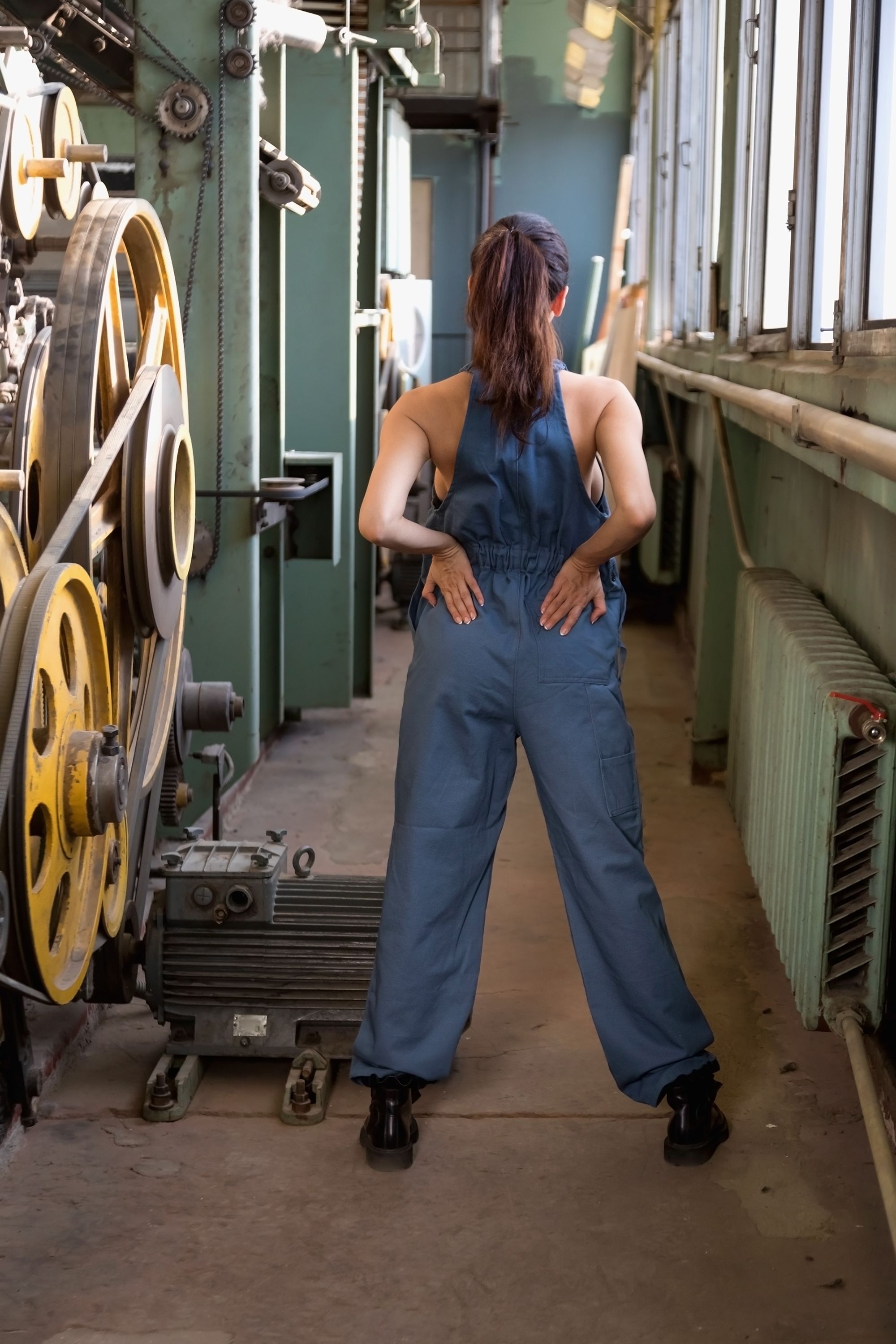 Frau in einem blauen Overall dreht den Rücken zur Kamera