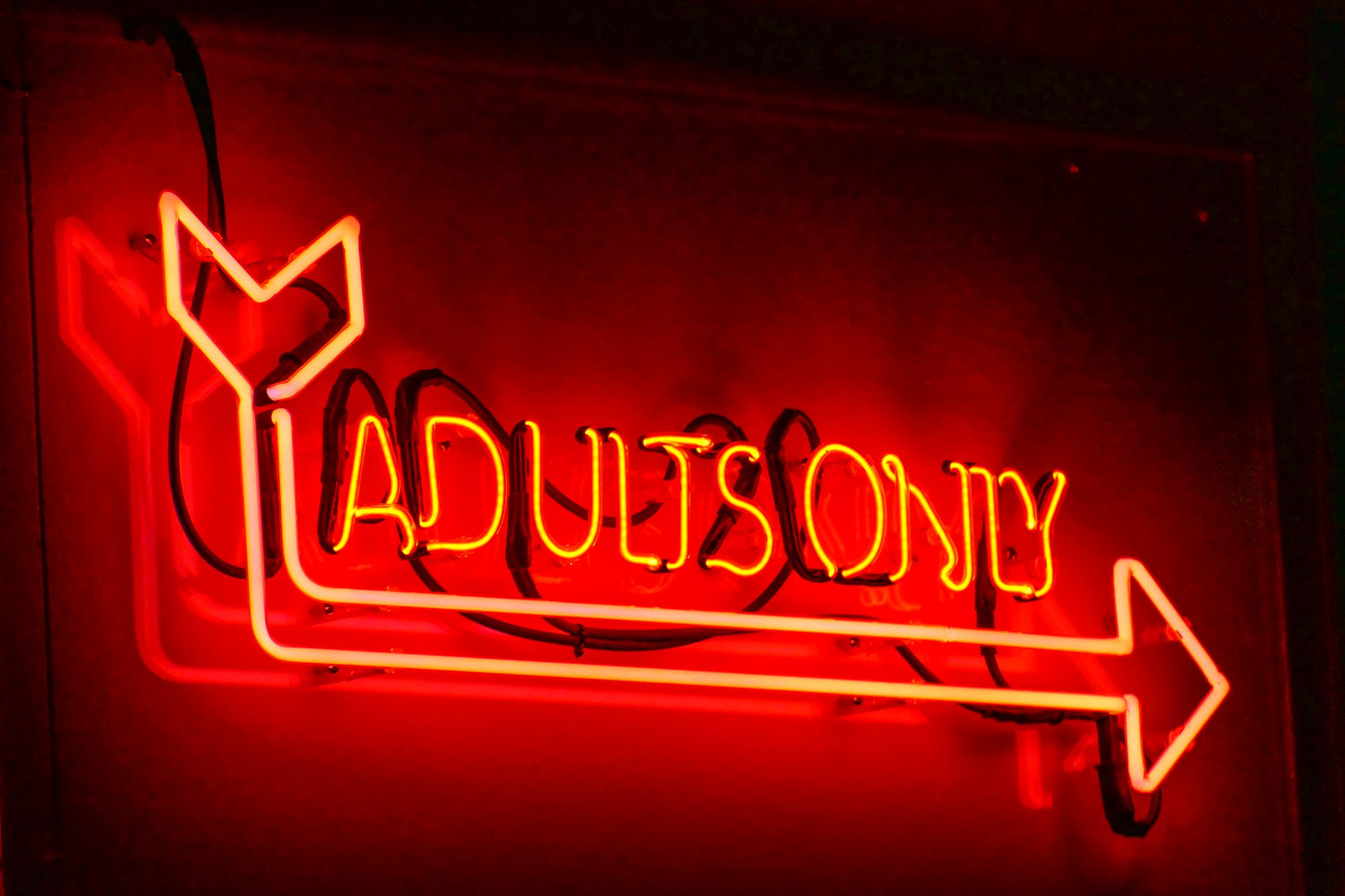 Rotes Leuchtschild mit der Aufschrift "Adults Only" und einem Pfeil darunter, welches an der Wand montiert ist