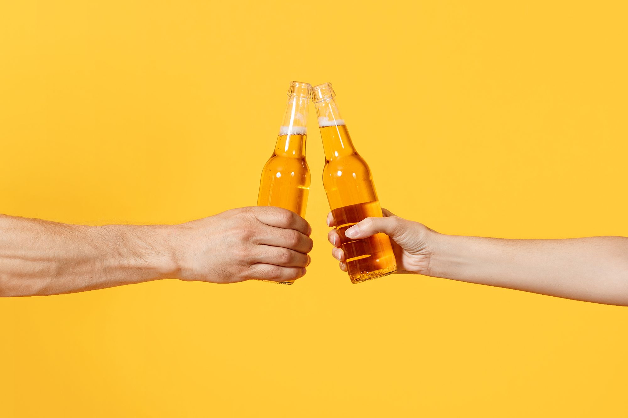 Zwei Hände vor einem gelben Hintergrund die mit Bier anstoßen