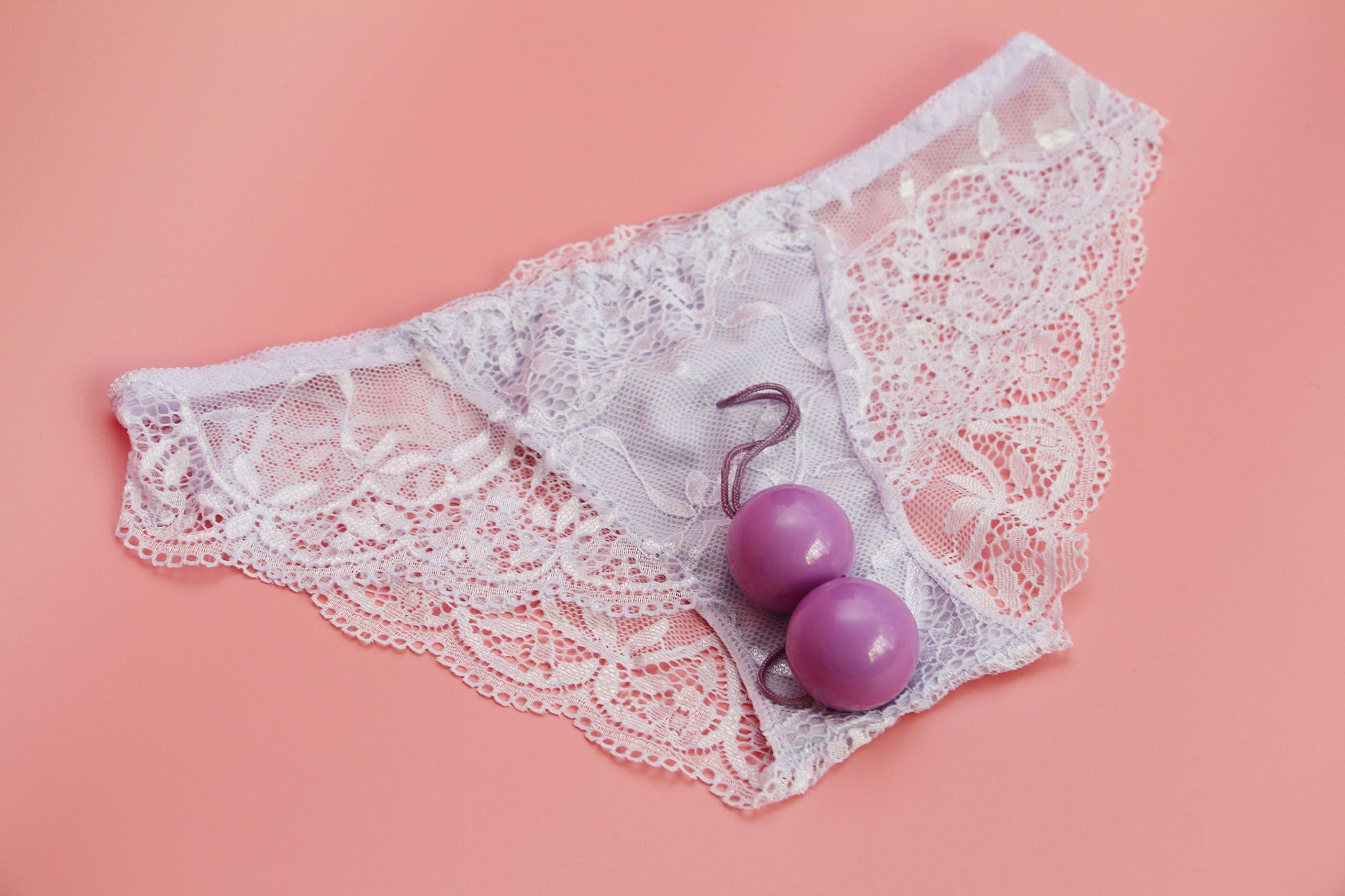 Pinke Liebeskugeln auf einem weißen Slip vor flamingofarbenem Hintergrund