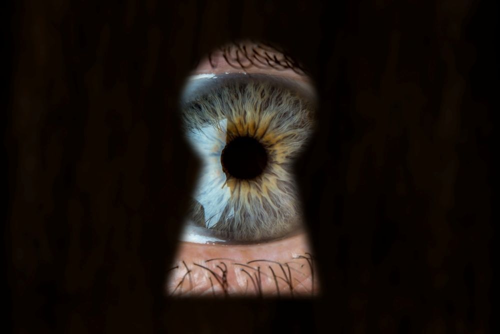 Eine Person mit blauen Augen späht durch ein Schlüsselloch.