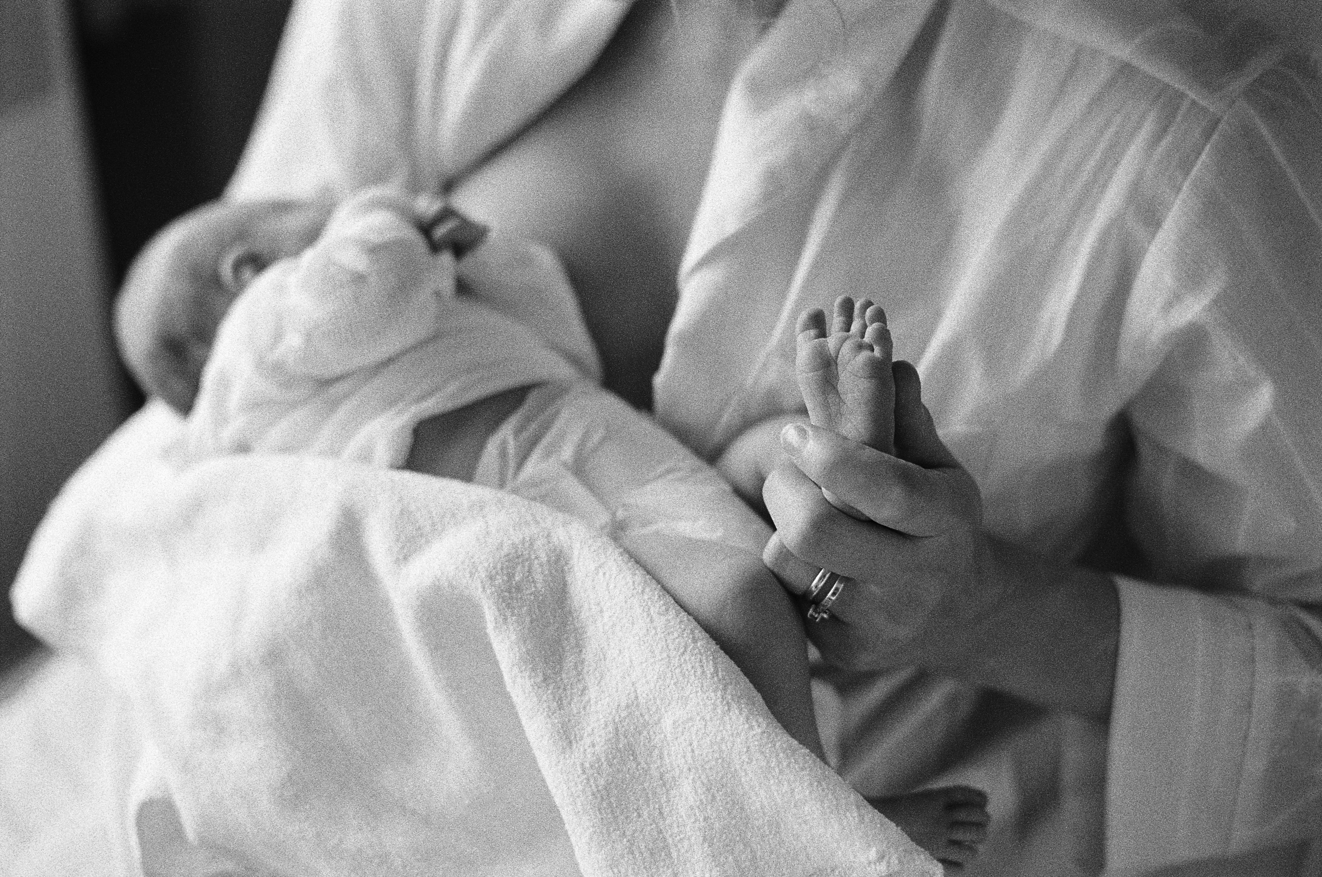 Eine Frau die ihr Baby stillt und dabei den Fuß des Babys in der Hand hält in schwarz-weiß