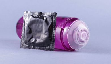 Ein lila Analgleitgel und ein Kondom vor einem pastell-lila Hintergrund