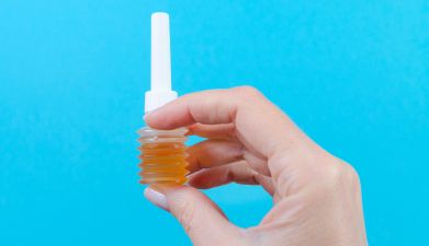 Eine Hand die eine Analdusche hält vor einem blauen Hintergrund