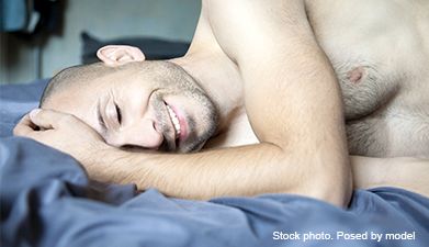 Ein Mann mit geschlossenen Augen, der seitlich auf einem Bett liegt und lächelt.