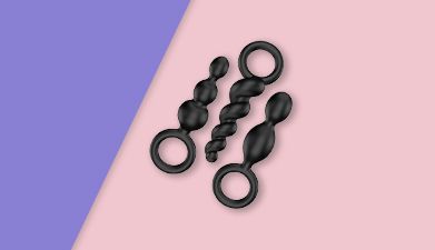 Schwarzes Analplug-Set Satisfyer 'Booty Call' auf lila-rosa geteiltem Hintergrund