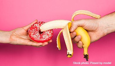 Zwei Hände die eine Banane und einen roten Donut halten vor einem pinken Hintergrund