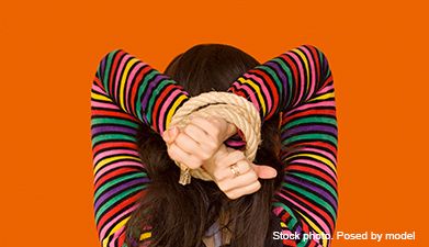 Eine Frau im bunt gestreiften Pullover mit gefesselten Händen die sie über ihren Kopf hält von hinte