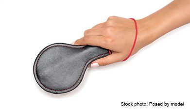 Eine Hand die ein schwarzes rundes BDSM-Paddle in der Hand hält vor einem weißen Hintegrund