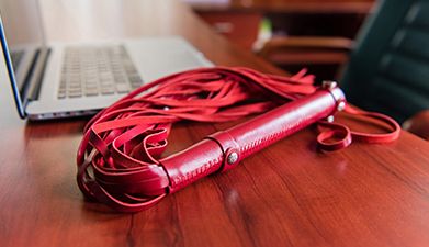 Eine rote Peitsche die auf einem Tisch liegt auf dem im Hintergrund ein Laptop steht