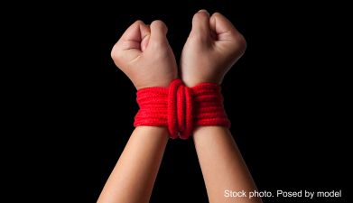 Hände die mit einem roten Bondage Seil gefesselt sind vor einem schwarzen Hintergrund