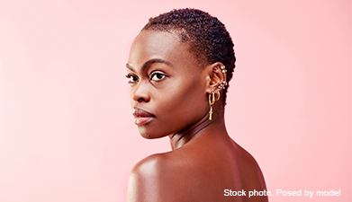 Eine dunkelhäutige Frau mit nichts bekleidet außer vielen Piercings an ihrem Ohr vor rosanem Hinterg