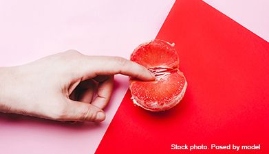 Ein Finger der eine gepellte halbe Blutorange berührt auf rot und rosafarbenem Hintergrund