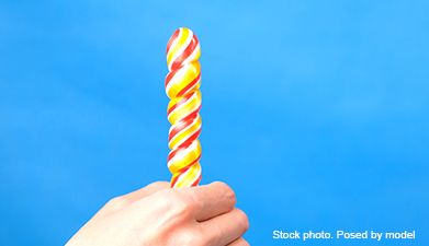 Eine Hand die einen gelb-orange-roten gedrehten Glasdildo hält vor einem blauen Hintergrund