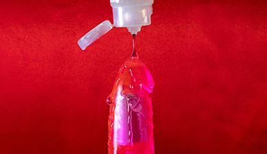 Gleitgel das aus einer Tube über einen roten Dildo läuft auf roten Hintergrund