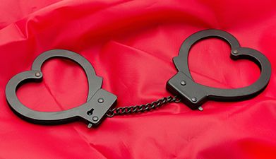 Schwarze Handschellen in Herzform vor rotem Hintergrund