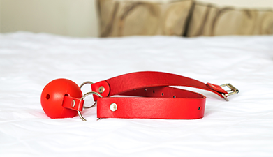 Ein roter Knebel, der auf einem Bett mit weißer Bettwäsche liegt.
