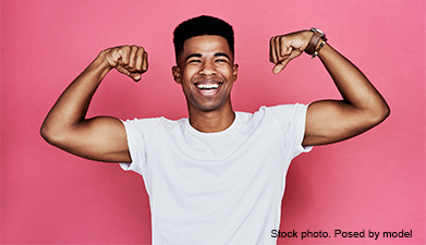 Ein Mann in einem weißen T-Shirt der seine Muskeln spielen lässt und dabei lachend in die Kamera sch