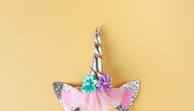 Ein Einhorn-Haarreif mit zwei Blüten drauf in Silber, Rosa und Glitzer vor einem gelben Hintergrund