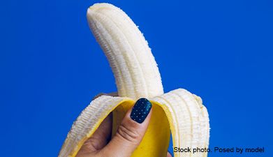 Eine Hand die eine halb geschälte Banane hält vor einem blauen Hintergrund