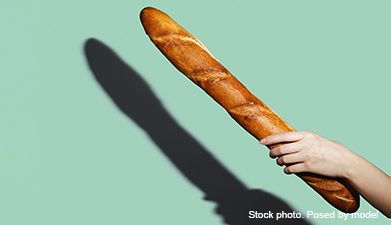 Eine Hand, die ein Baguette in die Luft hält vor einem mint-grünen Hintergrund