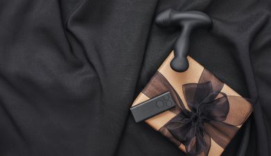 Ein Geschenk neben dem ein schwarzer Prostata Vibrator liegt vor einem schwarzen Hintergrund