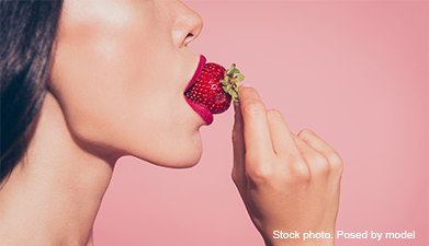 Das Profil einer Frau, die gerade in eine Erdbeere beißt vor einem rosanen Hintergrund