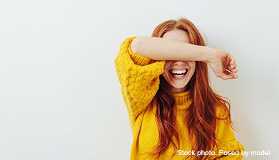 Eine Frau mit roten Haaren in einem gelben Pullover, die ihren rechten Arm vor ihre Augen hält und h