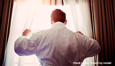 Ein Mann der vor einem Fenster steht und dabei die Gardinen zur Seite zieht