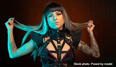 Eine alternativ in Leder-Dessous gekleidete Frau mit gefärbtem Haar posiert unter blauem Licht