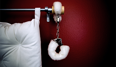 Ein Ausschnitt eines Bettes an dessen Kopfteil weiße Plüsch-Handschellen hängen