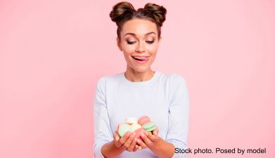Eine Frau mit Macarons in den Händen vor einem rosa Hintergrund