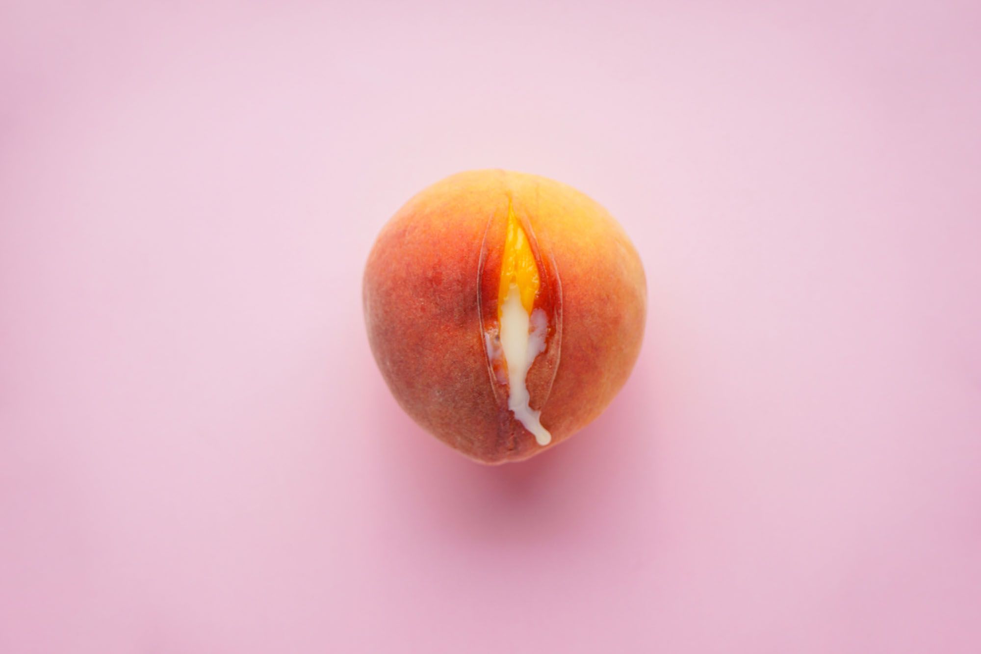 Ein Pfirsich vor rosanem Hintegrund aus dem eine weiße Flüssigkeit rausläuft