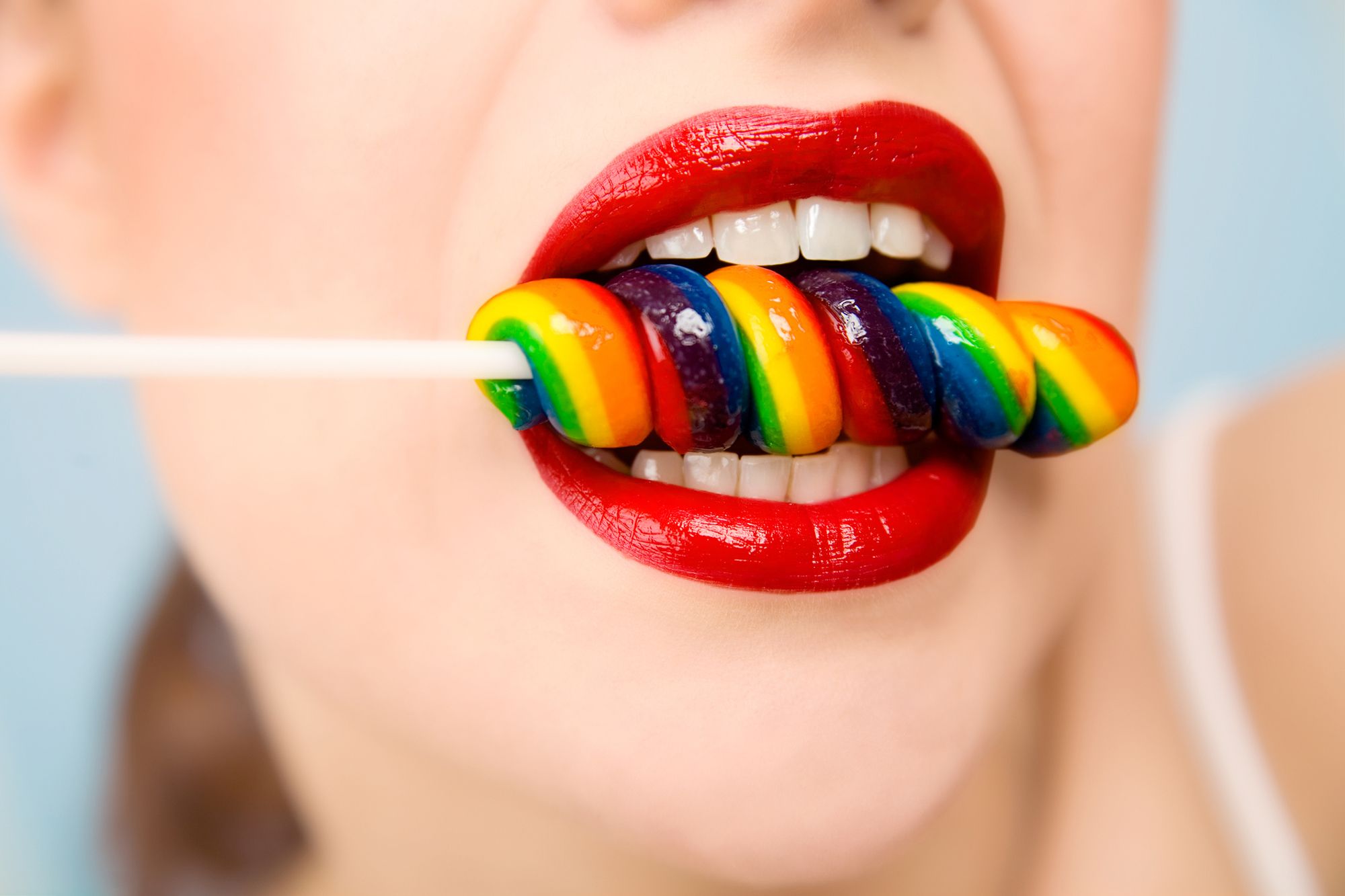 Frau hat einen Lolli mit Regenbogenmuster zwischen den Zähnen