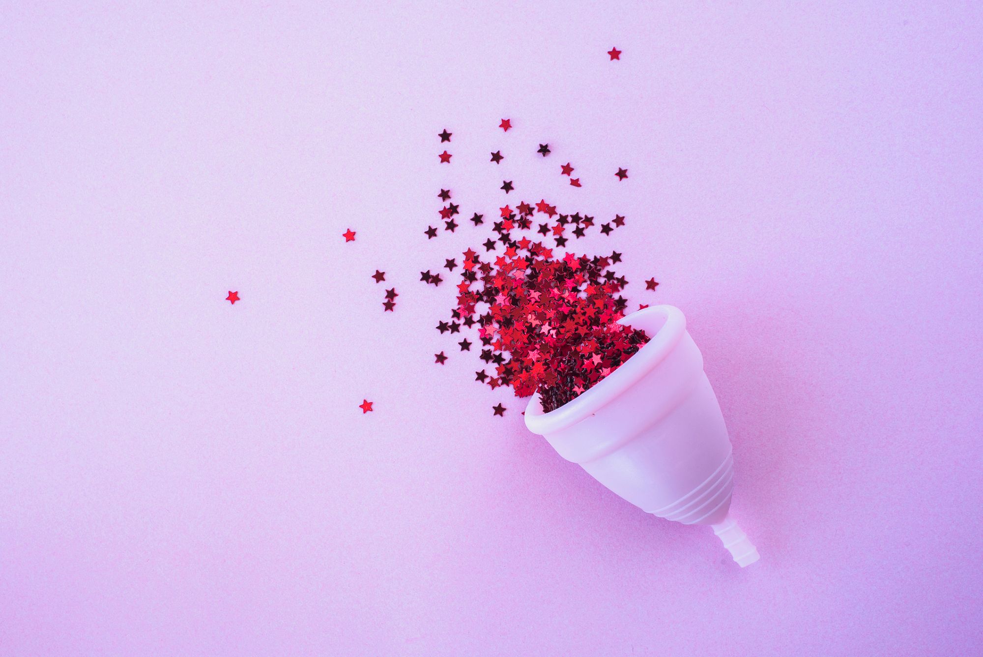 Rosane Menstruationstasse mit Sternenkonfetti auf rosa Hintergrund