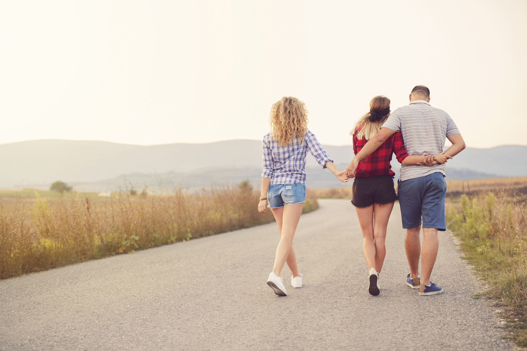 Mann hält beim spazieren gehen im Feld die Hände von zwei Frauen