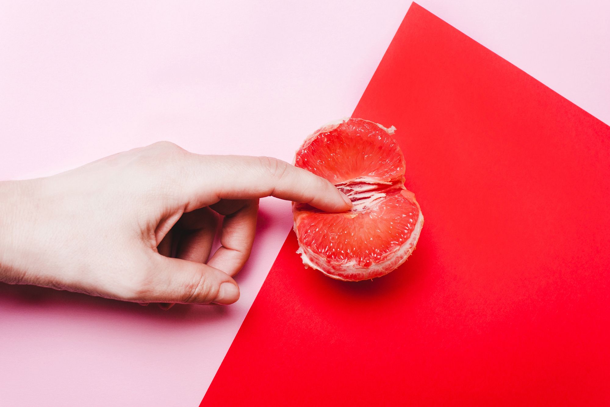 Finger in einer Grapefruit auf rot-rosa Hintergrund