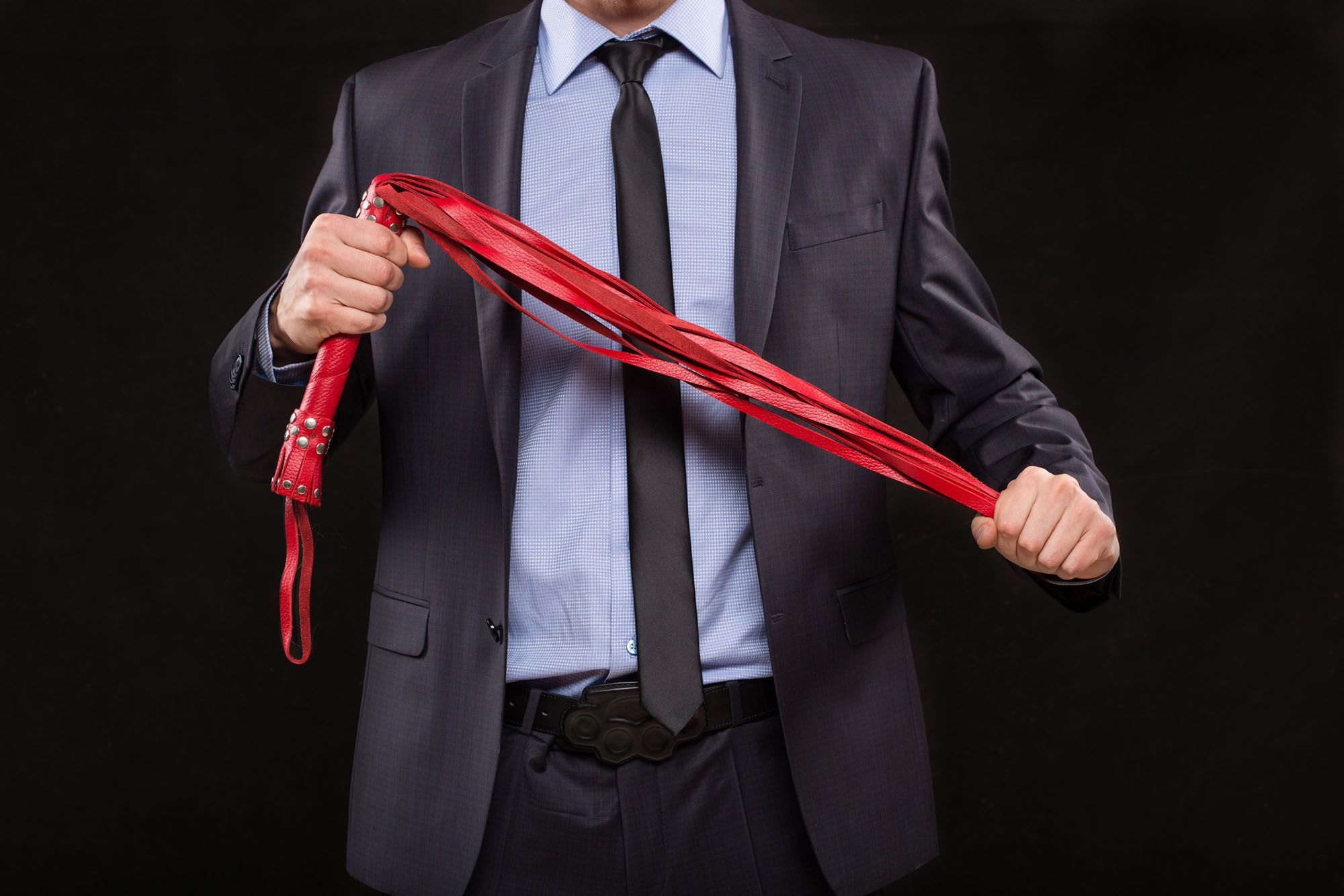 Mann im Anzug hält eine rote Peitsche in den Händen