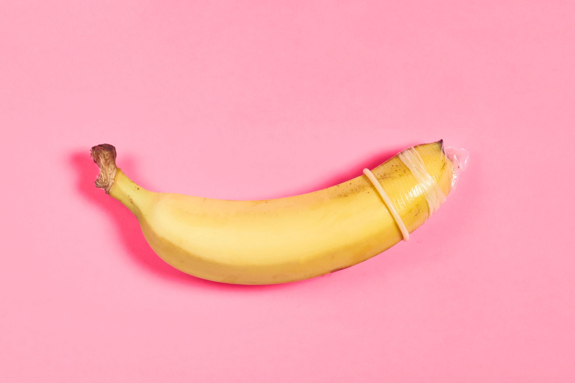 Banane mit Kondom auf pinkem Hintergrund
