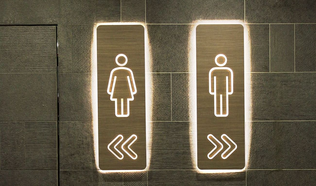 Gang, in dem ein Schild Richtung Damentoilette und eins Richtung Herrentoilette zeigt