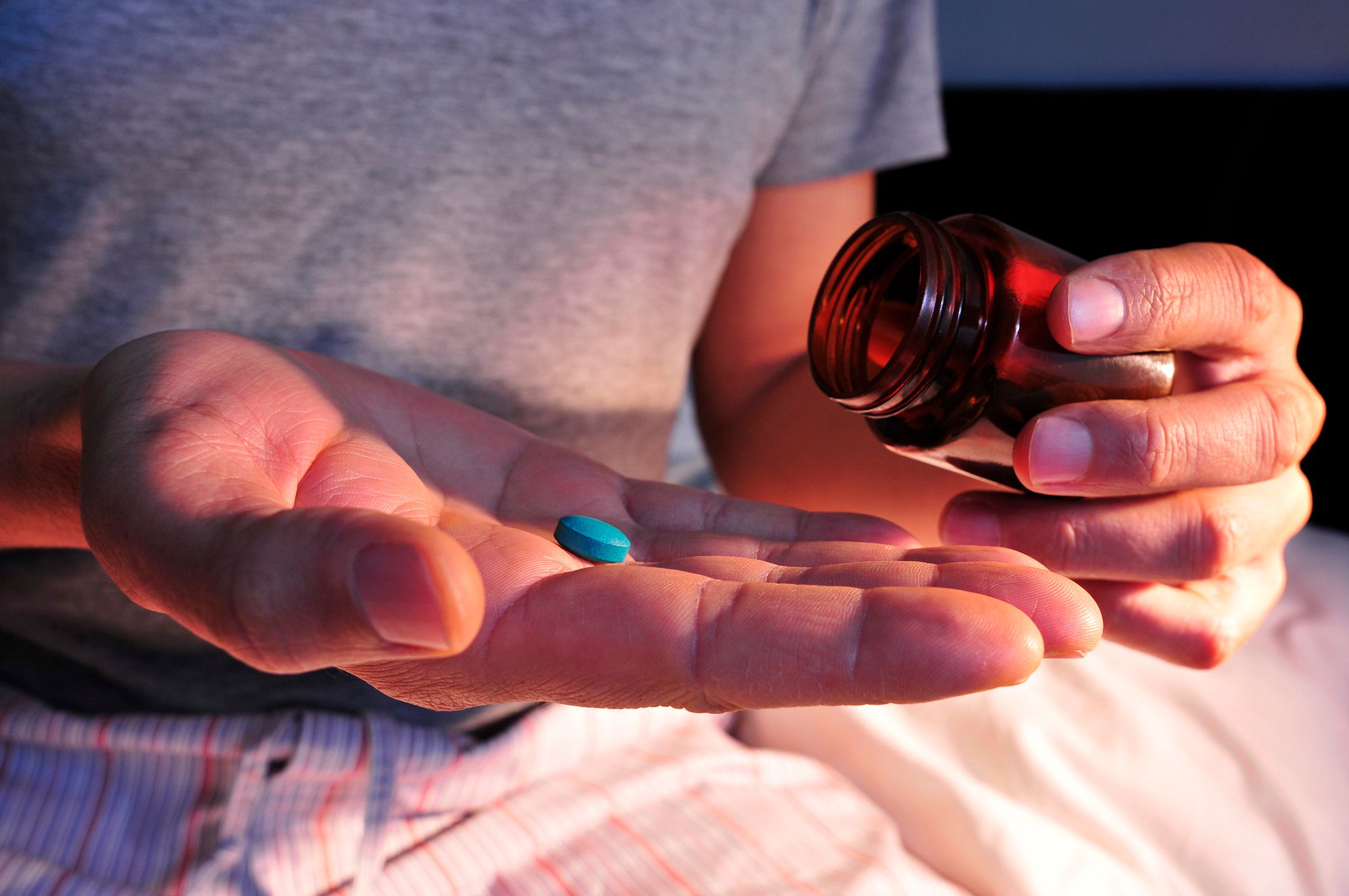 Mann hält ein Gefäß und eine blaue Pille in der Hand